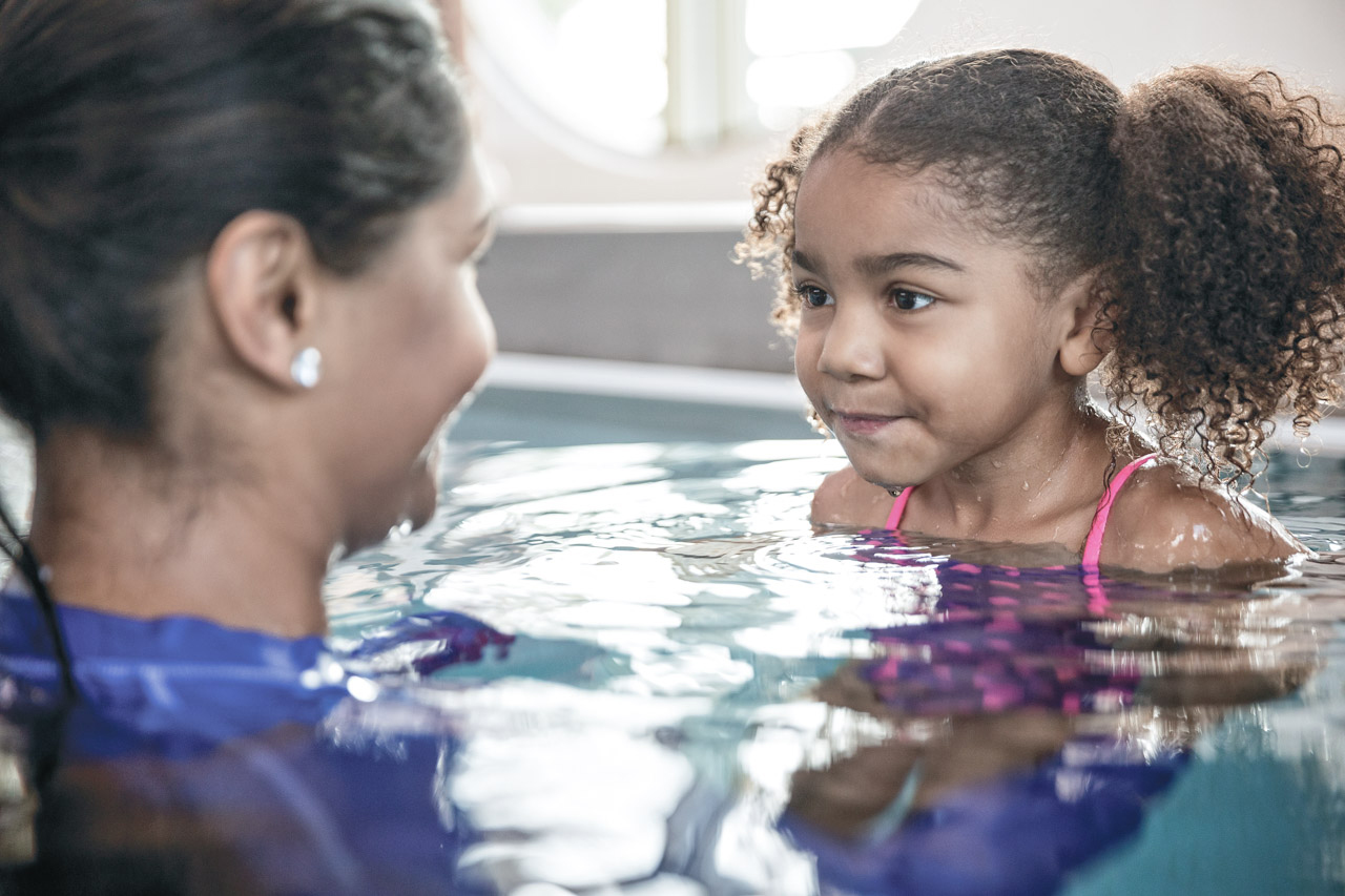 A elementary aged girl is in the pool getting a swim lesson