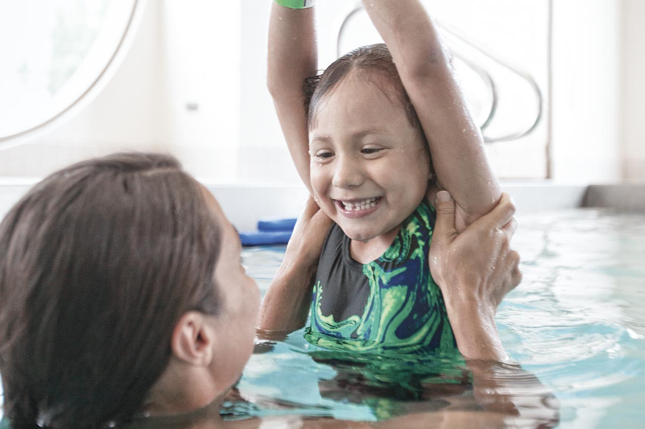 A closeup of a swim instructor helping a young girl float in an indoor pool