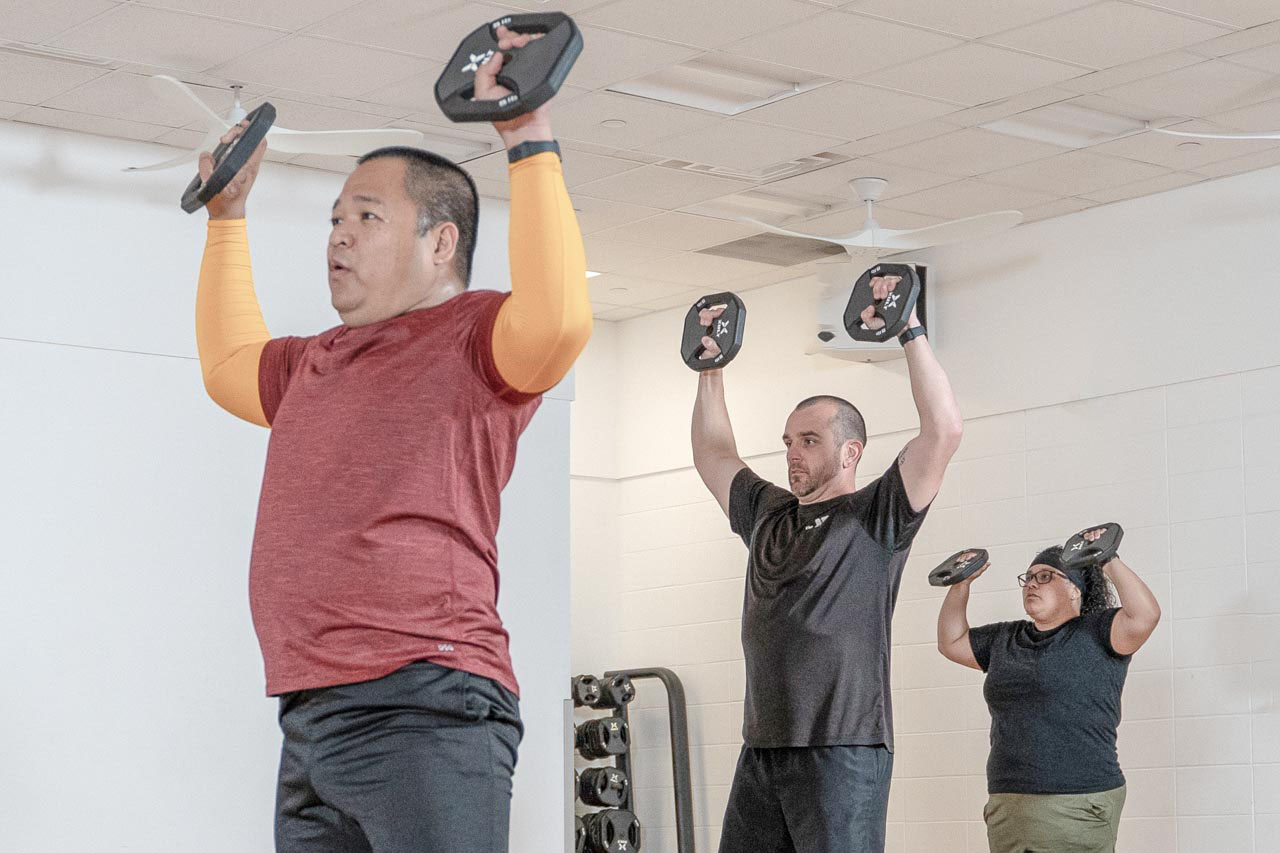 A group of three men lift weights over their heads