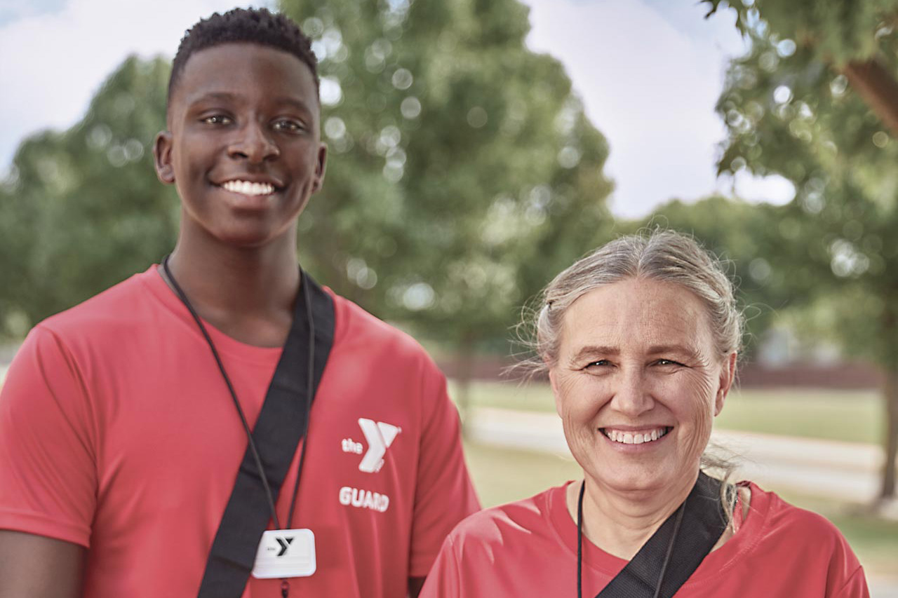 Two lifeguards in red shirts stand and smile into the camera