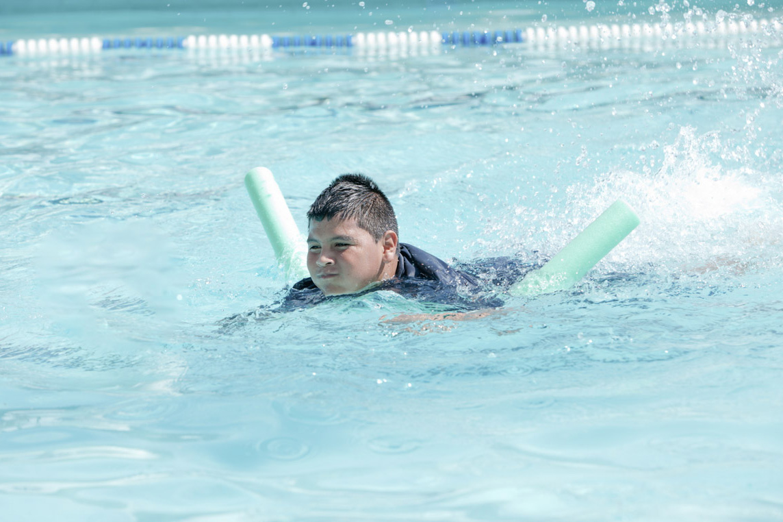 A middle school paged boy practices kicking in the pool with a pool noodle