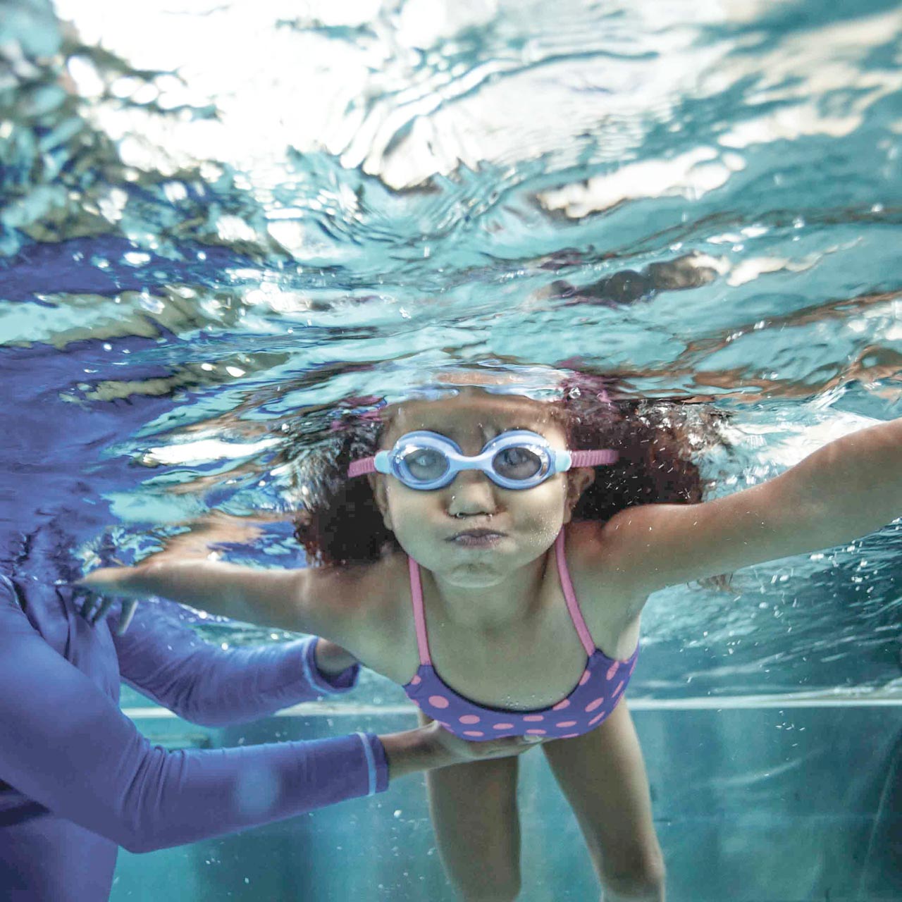 An underwater shot of a young girl puffing out her cheeks with air, learning the basics of swimming